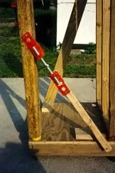 Red Scroogeclamp fastened to a wood post, with a board running from it down to a wooden platform as a diagonal brace